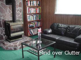 A family room with a fire place, black couch, bookcase and glass coffee table. 