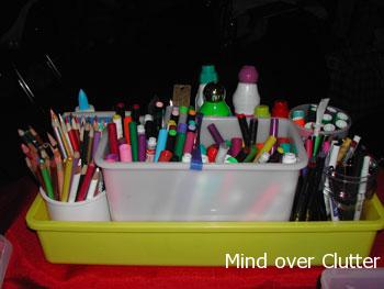 a yellow plastic container holding markers, pens, pencil, crayon, glue 