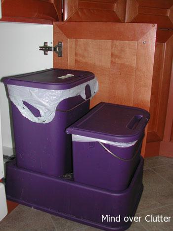 a pullout rack holding a blue garbage bin and a smaller blue recycling bin