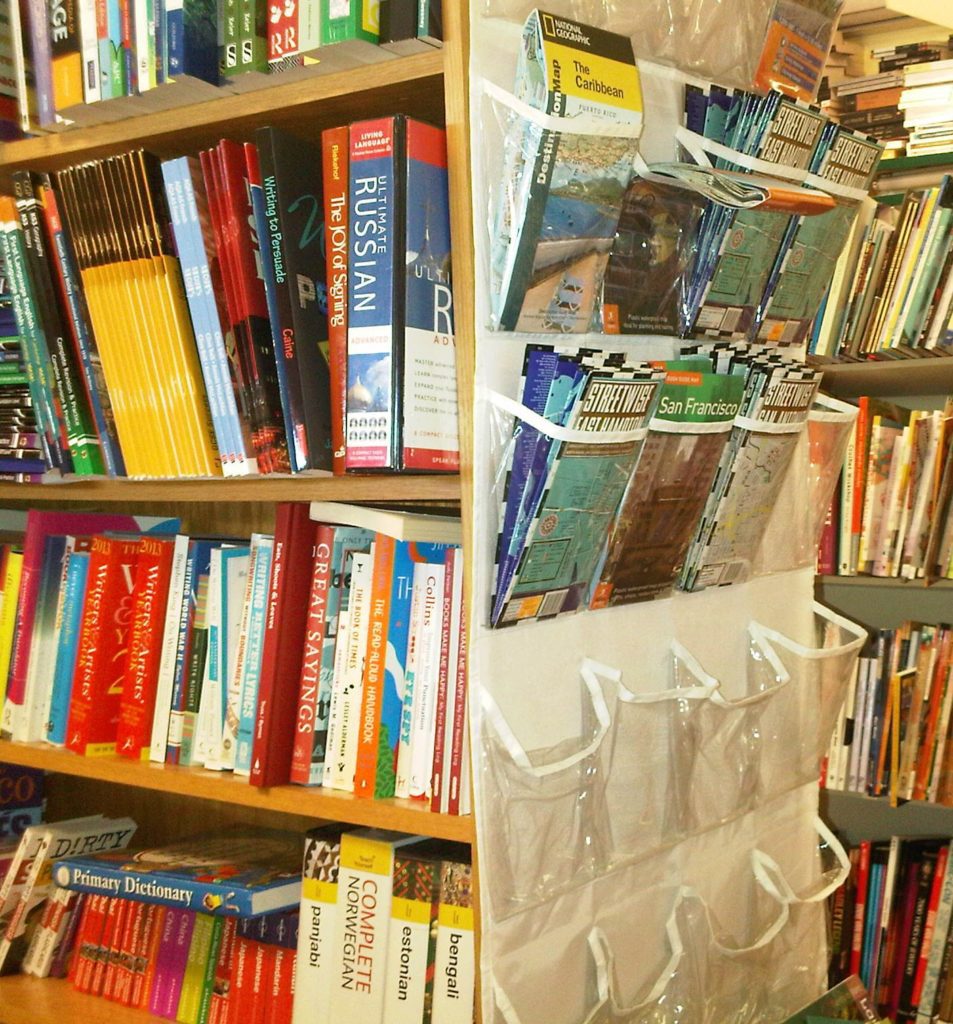 A white shoe organizer with clear pockets hanging on a bookcase with maps in the pockets