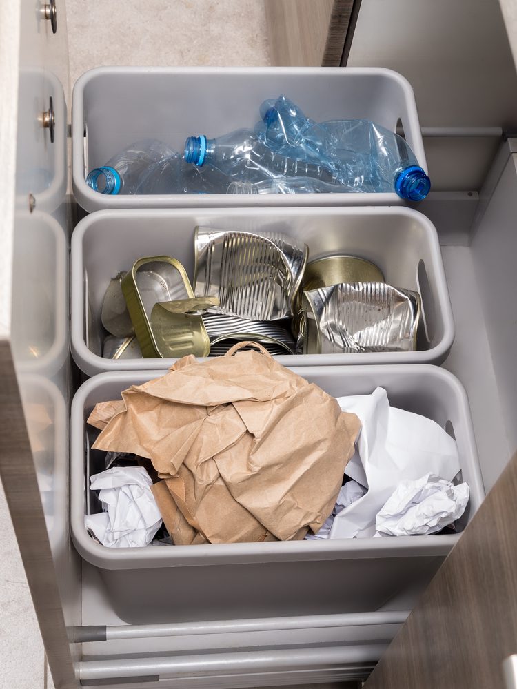 Three plastic trash bins in kitchen cabinet with segregated household garbage - PET bottles, paper and metal cans