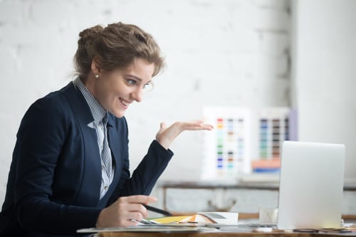 Portrait of young smiling shocked business woman wearing suit sitting at home office desk using laptop, looking at computer screen with happy surprised face expression, showing euphoric funny reaction
