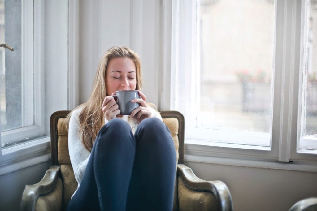 women isting on a chair with her knees up to her chest with a cup of coffee