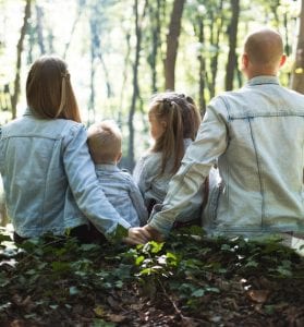 man and woman holding hands together with boy and girl looking at green trees during day