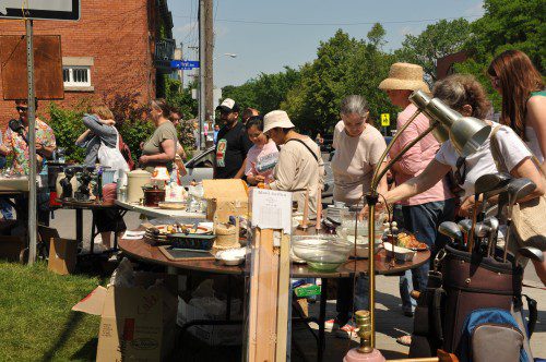 Tables set up with items for sale on a driveway. There are lots of people browsing. 