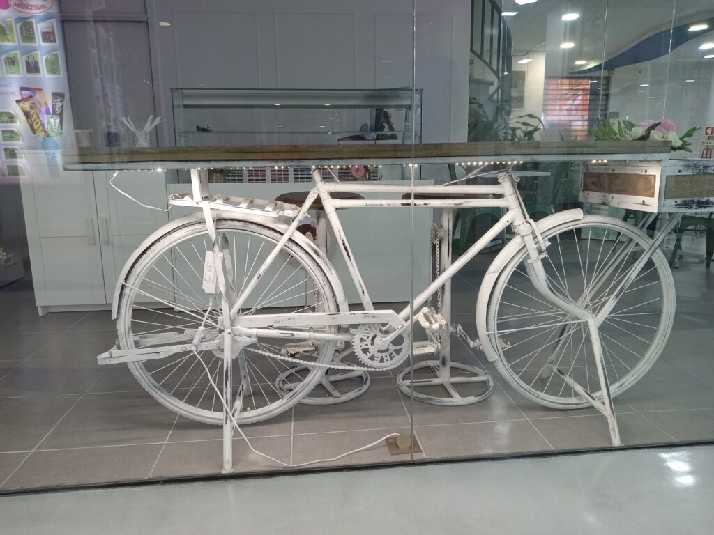 A bicycle painted white with a board mounted from seat to handle bars to make a table. 