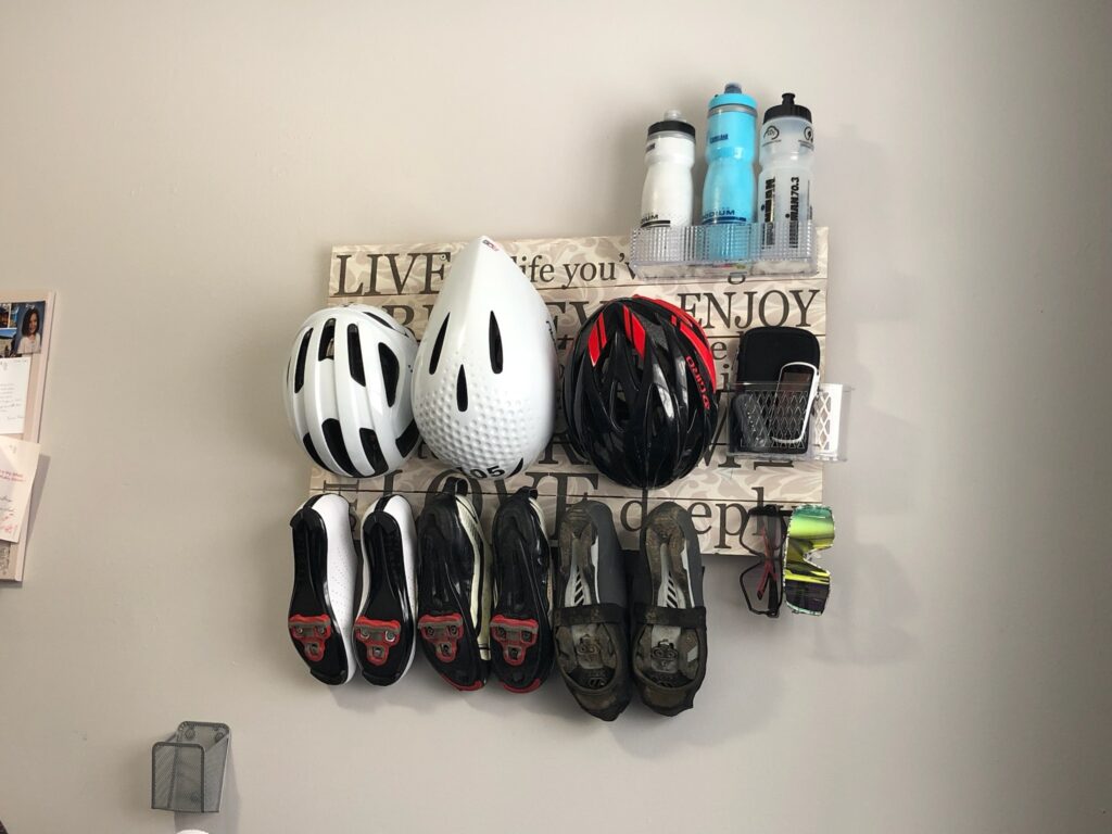 A wooden sign with hooks mounted on the wall to hold cycling gear. 