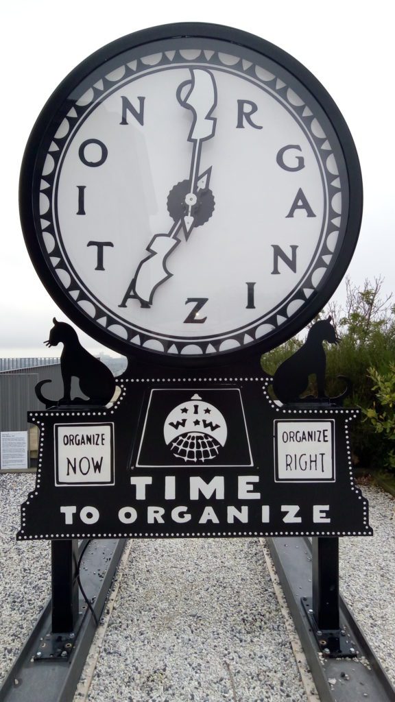 A metal sculture of a clock with the letters organizing on the face.