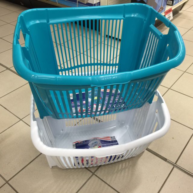 A plastic white laundry basket stacked ontop of a blue plastic laundry basket.
