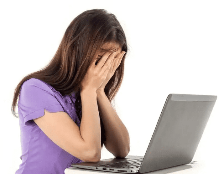 A lady bent over her computer with her hands covering her eyes