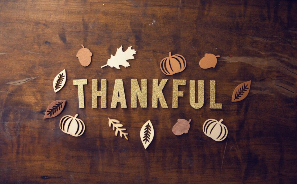 A wooden sign with the word Thankful surrounded by leaves, nuts, pumpkins.