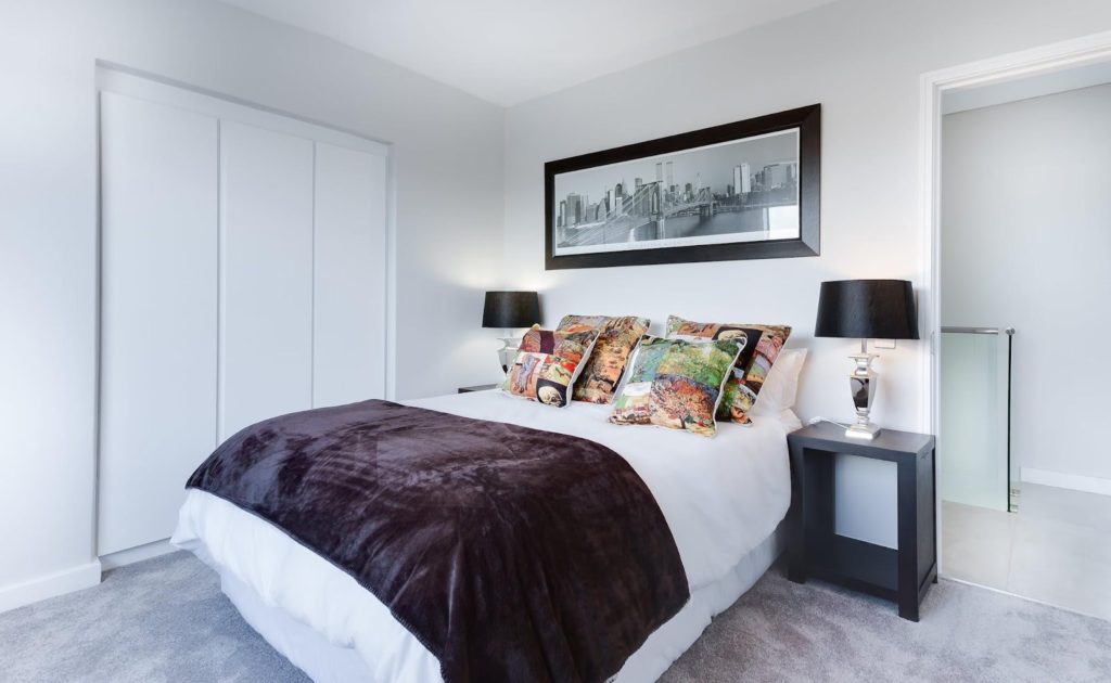 A bedroom with a queen size bed and 2 night table and a cityscape picture over the bed. 