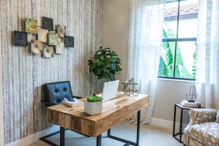 A wooden desk with a laptop and book on it with a black leather desk chair. 