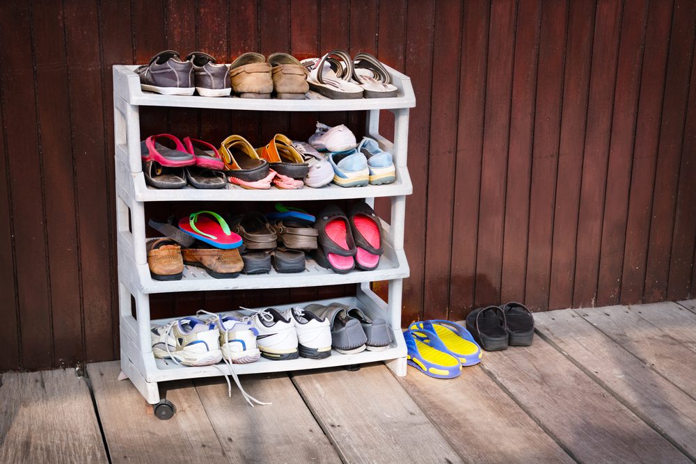 A variety of colorful shoes, neatly ordered on a plastic shoe rack outside a wooden house.