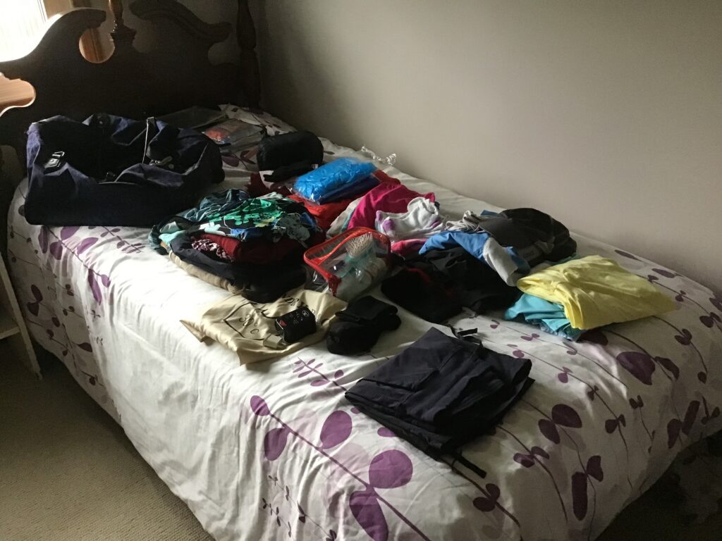 A single bed with clothing that will be taken on a trip. 