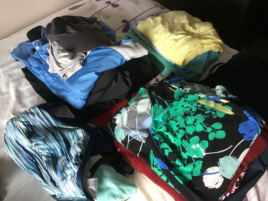 Piles of like clothing stack on a bed ready to be put into a suitcase. 